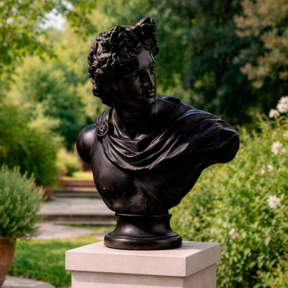 Busto di Apollo in bronzo scuro, copia dell’originale dei Musei Vaticani, con capelli scolpiti e mantello drappeggiato, fotografato in ambiente esterno con giardino.