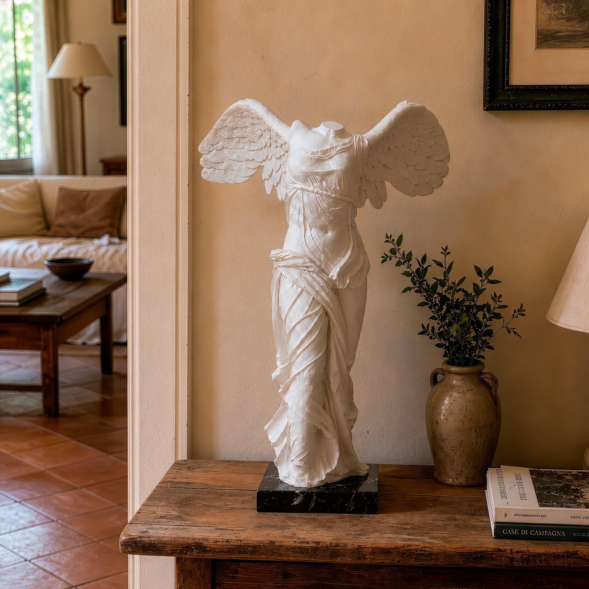 Riproduzione della Nike di Samotracia, statua classica in marmo bianco raffigurante una figura femminile alata senza testa e senza braccia, con panneggio mosso e ali spiegate, su base scura ,vista frontalmente