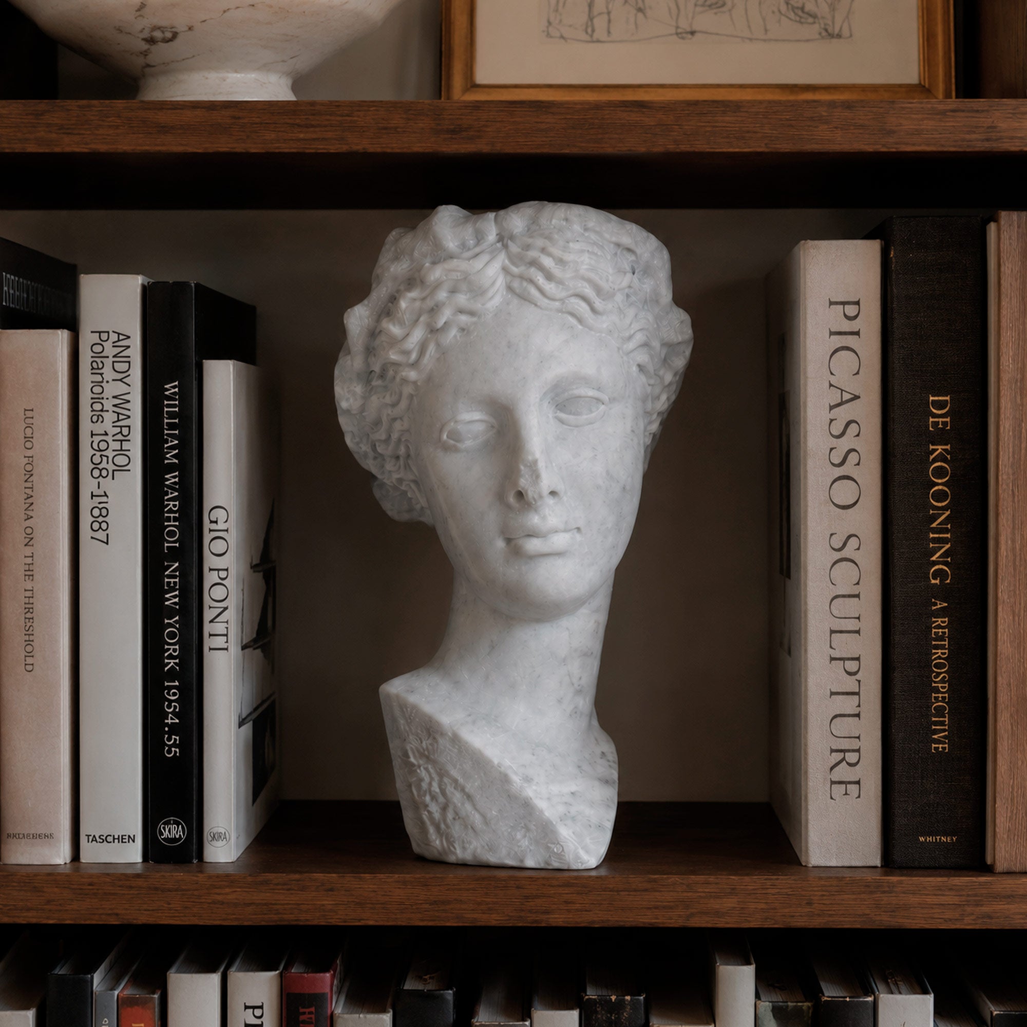 Bust of Thalia, Muse of Comedy, in white Carrara marble, front view in a library.