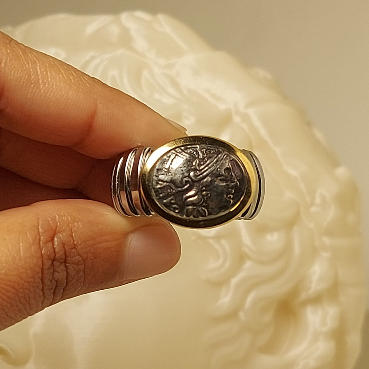 Anello con riproduzione di moneta antica e bordo dorato, tenuto tra le dita