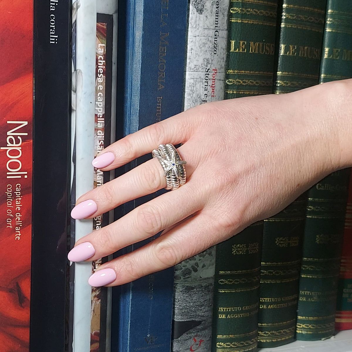 Anello a sei giri con stella marina, indossato sulla mano appoggiata a libri