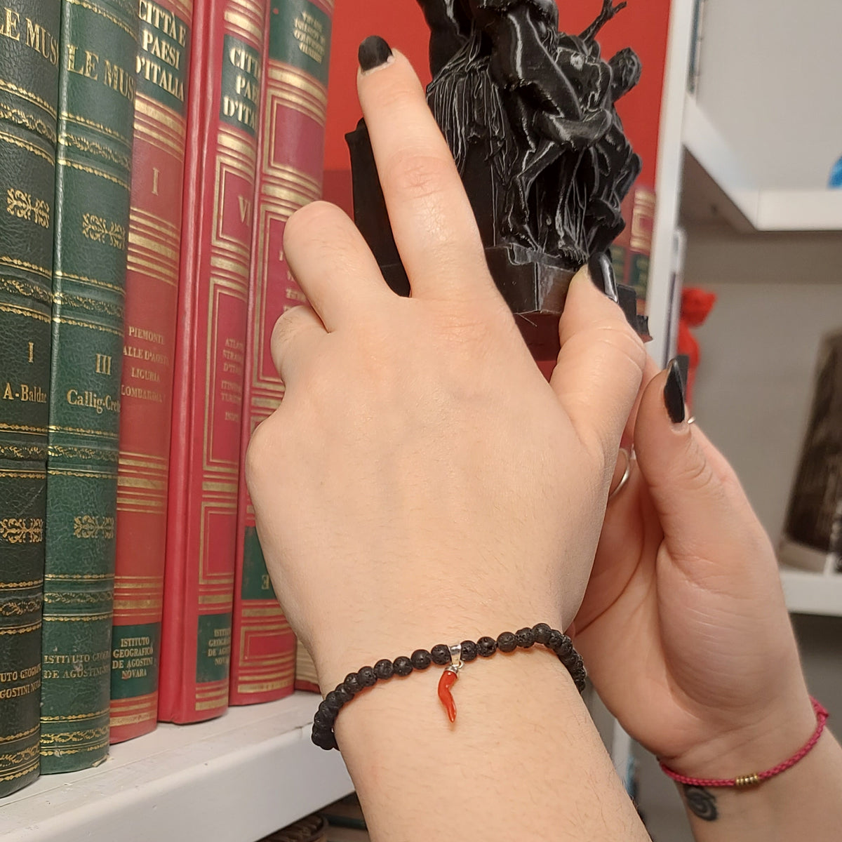 Bracciale in pietra lavica con corno rosso e attacco in argento, indossato al polso davanti a una libreria