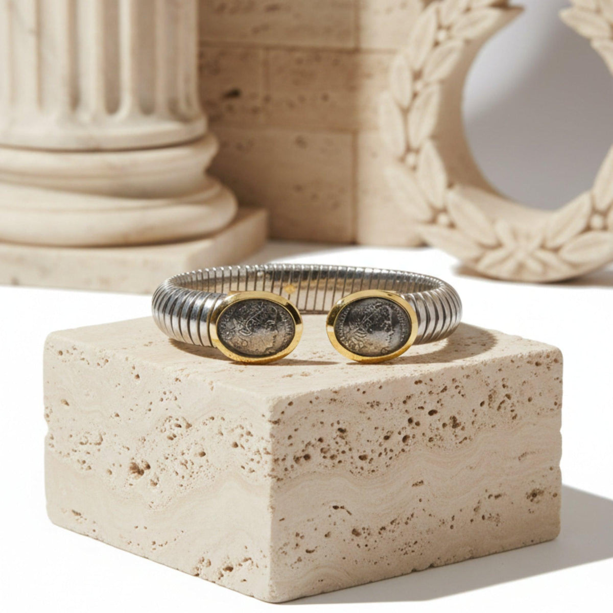 Bracciale aperto con due repliche di monete antiche in cornici dorate, su un supporto in pietra