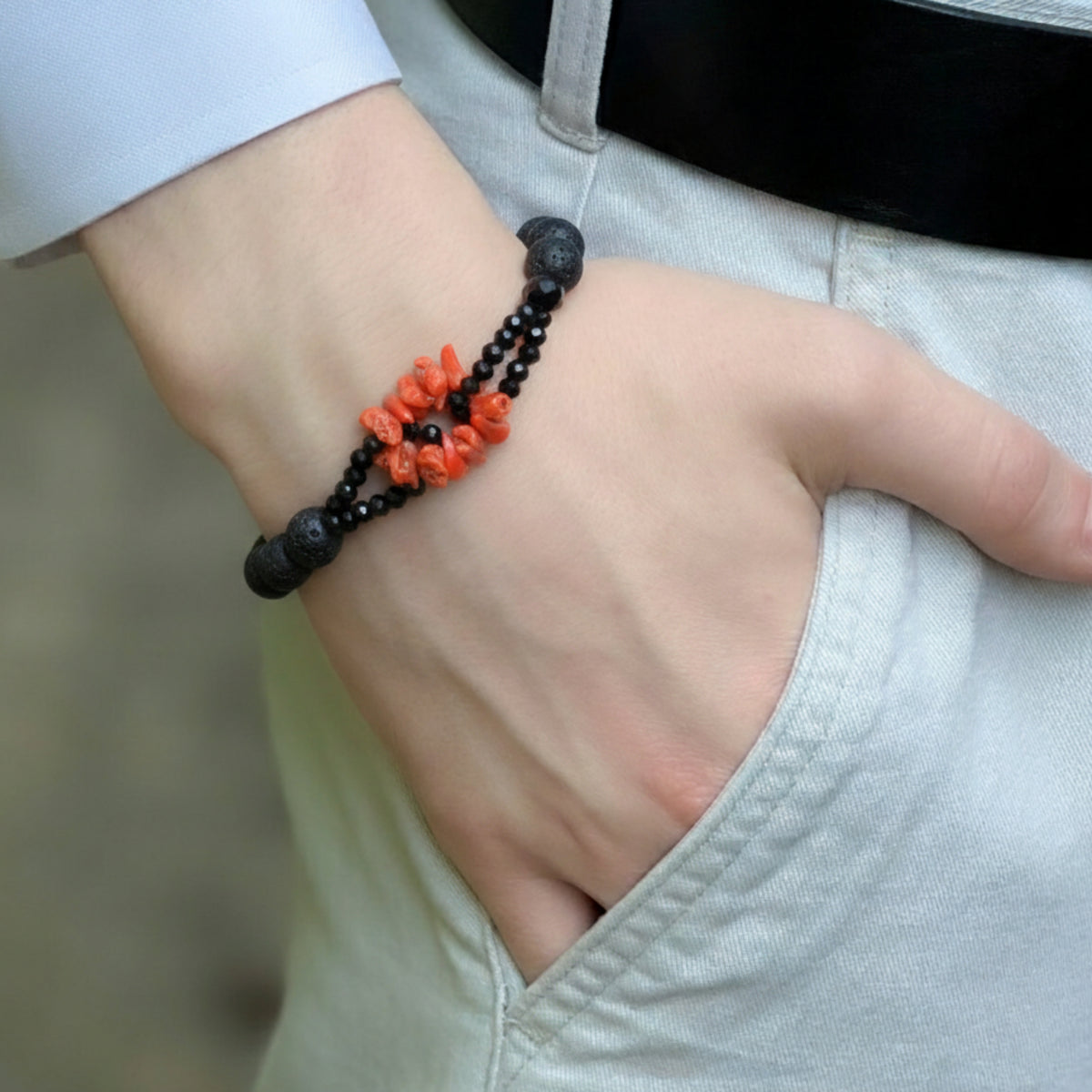 Bracciale con scaglie di corallo rosso, pietra lavica e onice, indossato al polso accanto a una camicia chiara