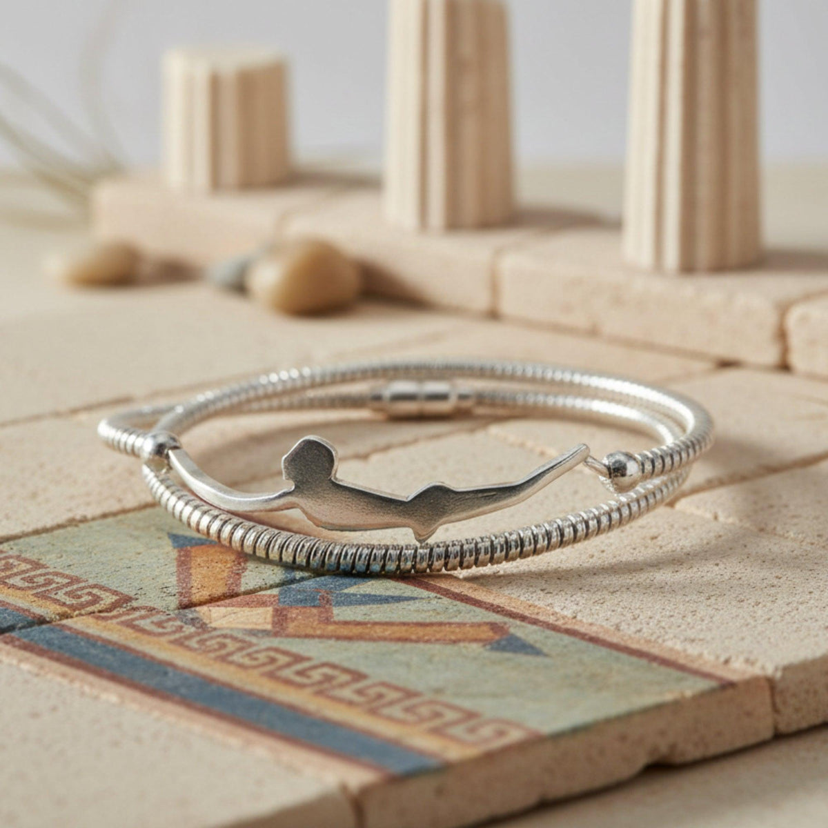 Bracciale a doppio giro in argento con sagoma del Tuffatore di Paestum, su un piano decorato