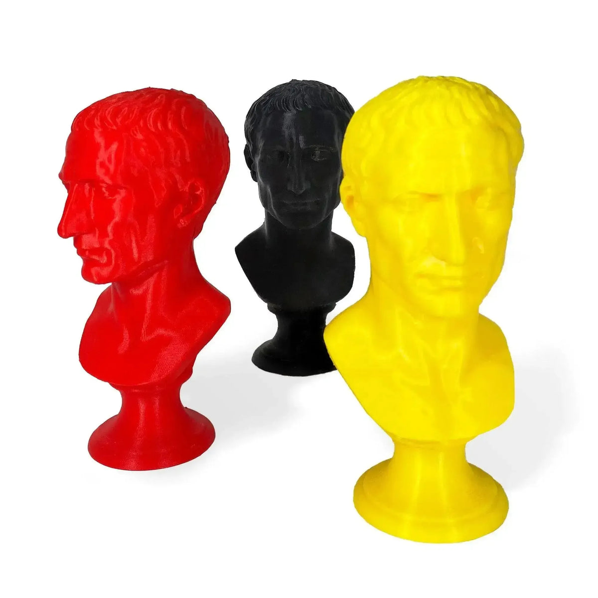 Tre busti di Giulio Cesare stampati in 3D nei colori rosso, nero e giallo, su fondo bianco.