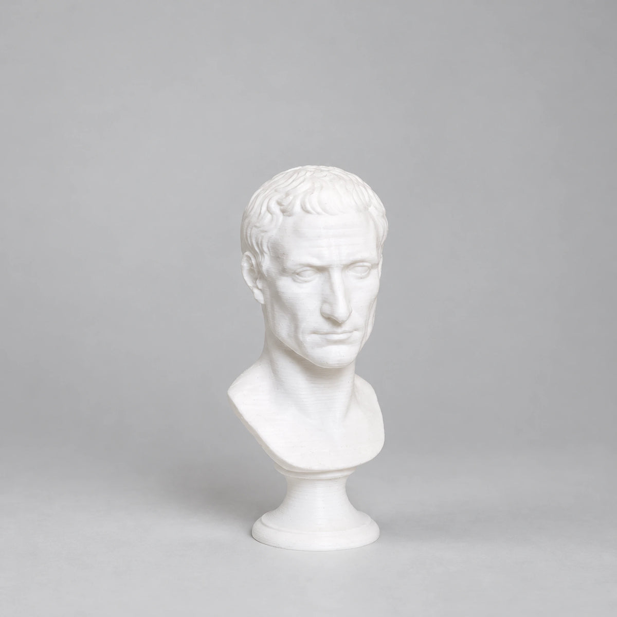 Busto di Giulio Cesare stampato in 3D in PLA bianco, su fondo grigio chiaro.