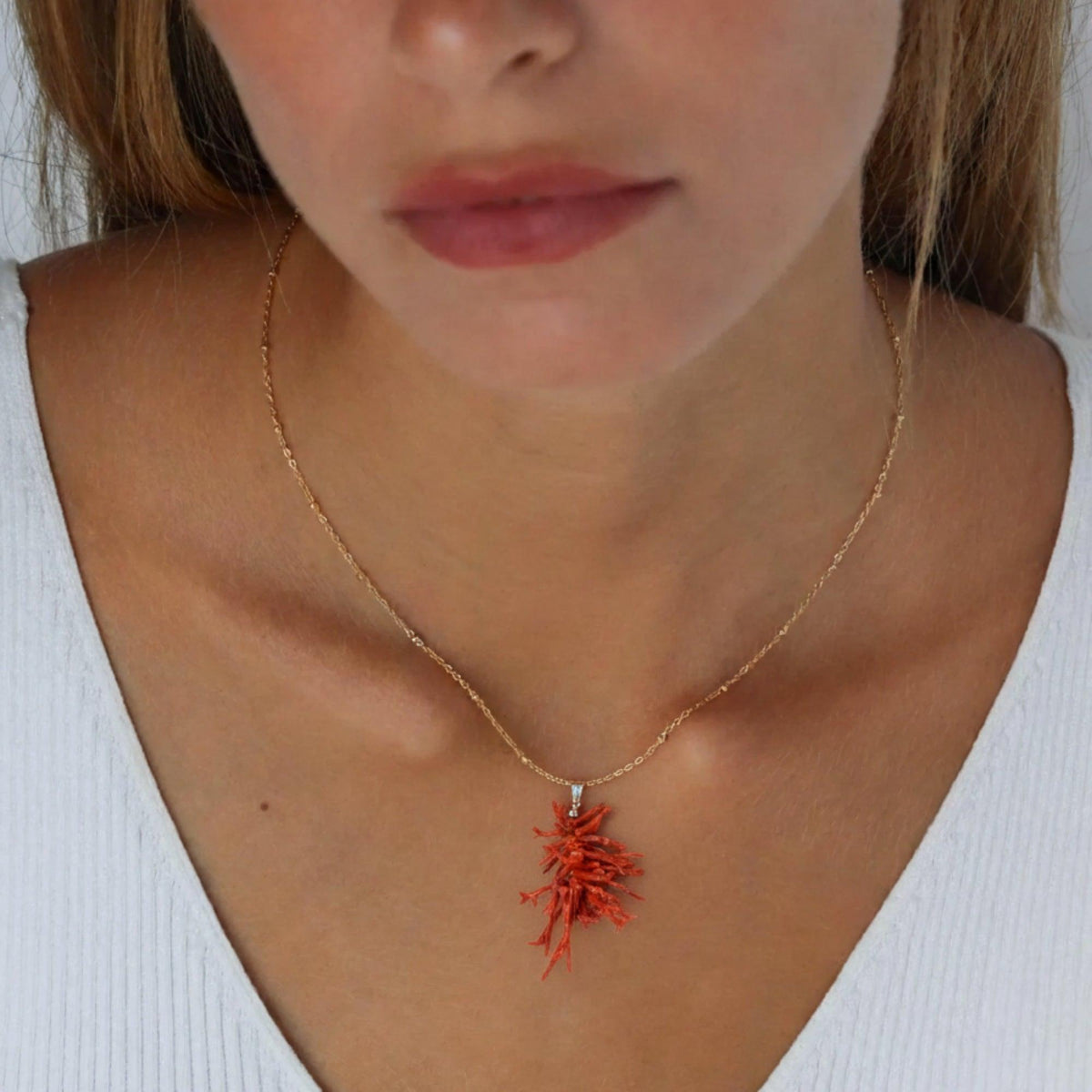Ciondolo con rami di corallo rosso e passante in argento, indossato con una maglia bianca