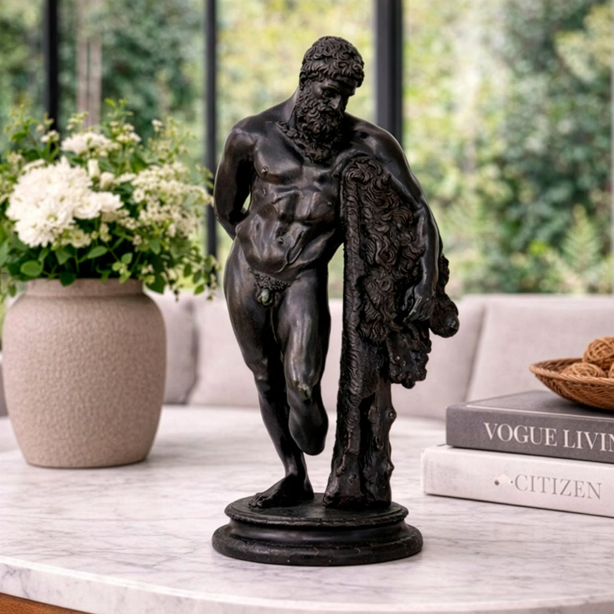 Ercole Farnese in bronzo scuro esposto in un soggiorno, accanto a un vaso con fiori bianchi e a libri.