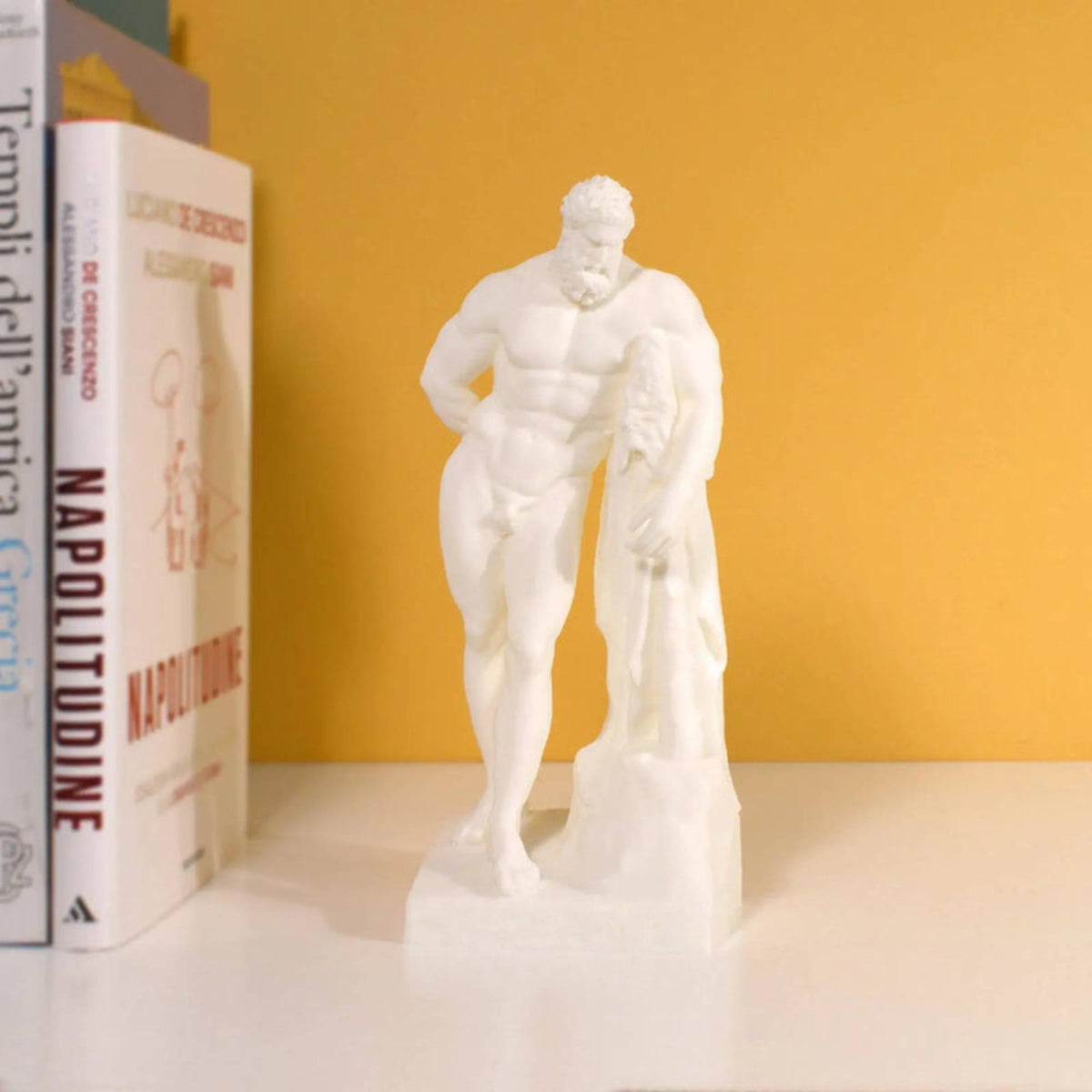 Ercole Farnese stampato in 3D bianco, su una mensola accanto a libri e parete gialla.