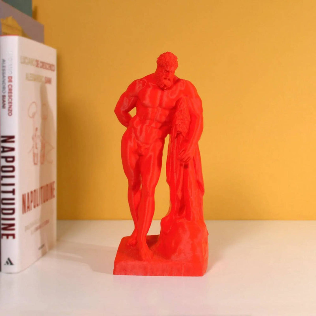 Ercole Farnese stampato in 3D rosso, su una mensola accanto a libri e parete gialla.