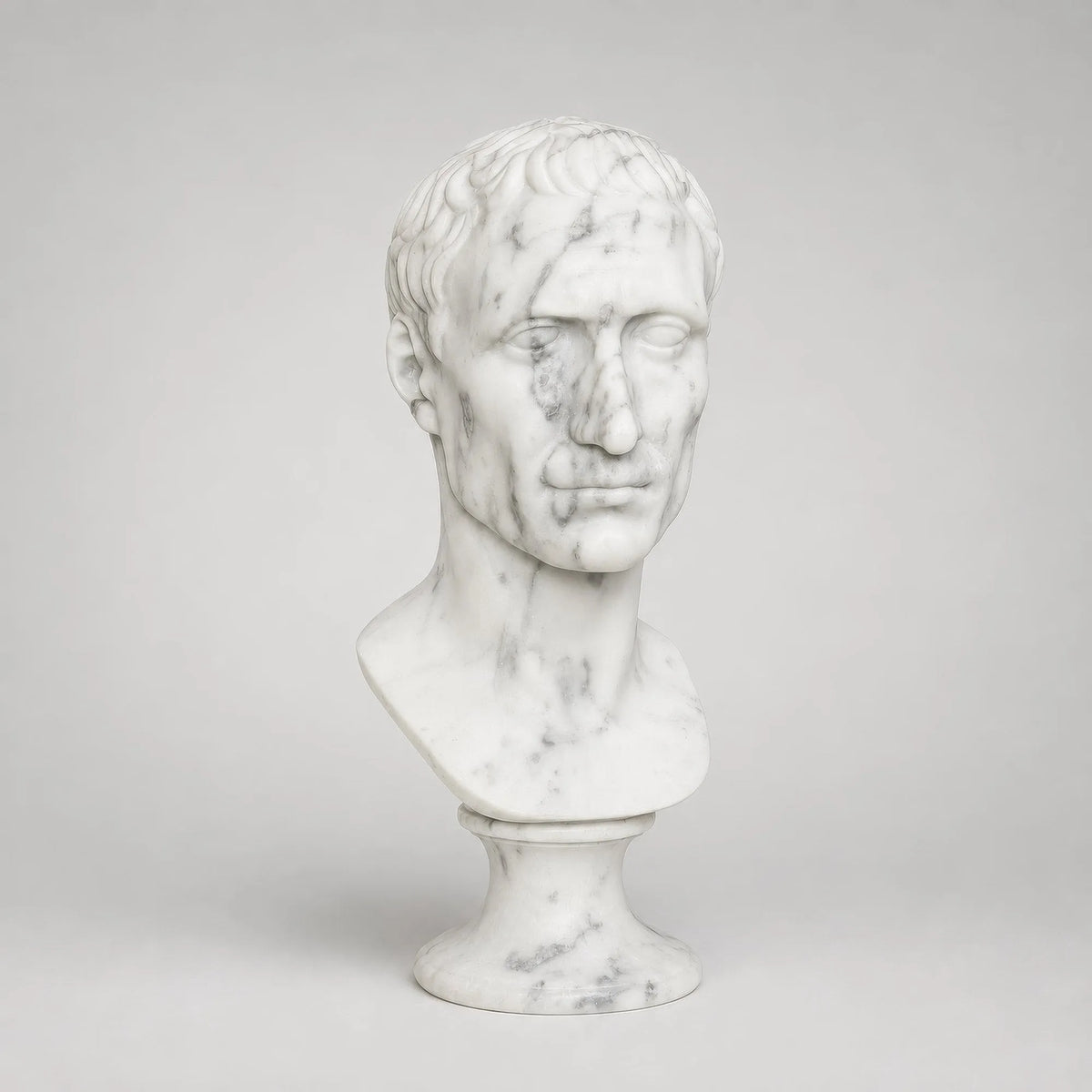 Busto di Giulio Cesare in marmo di Carrara, vista di tre quarti su fondo grigio chiaro.