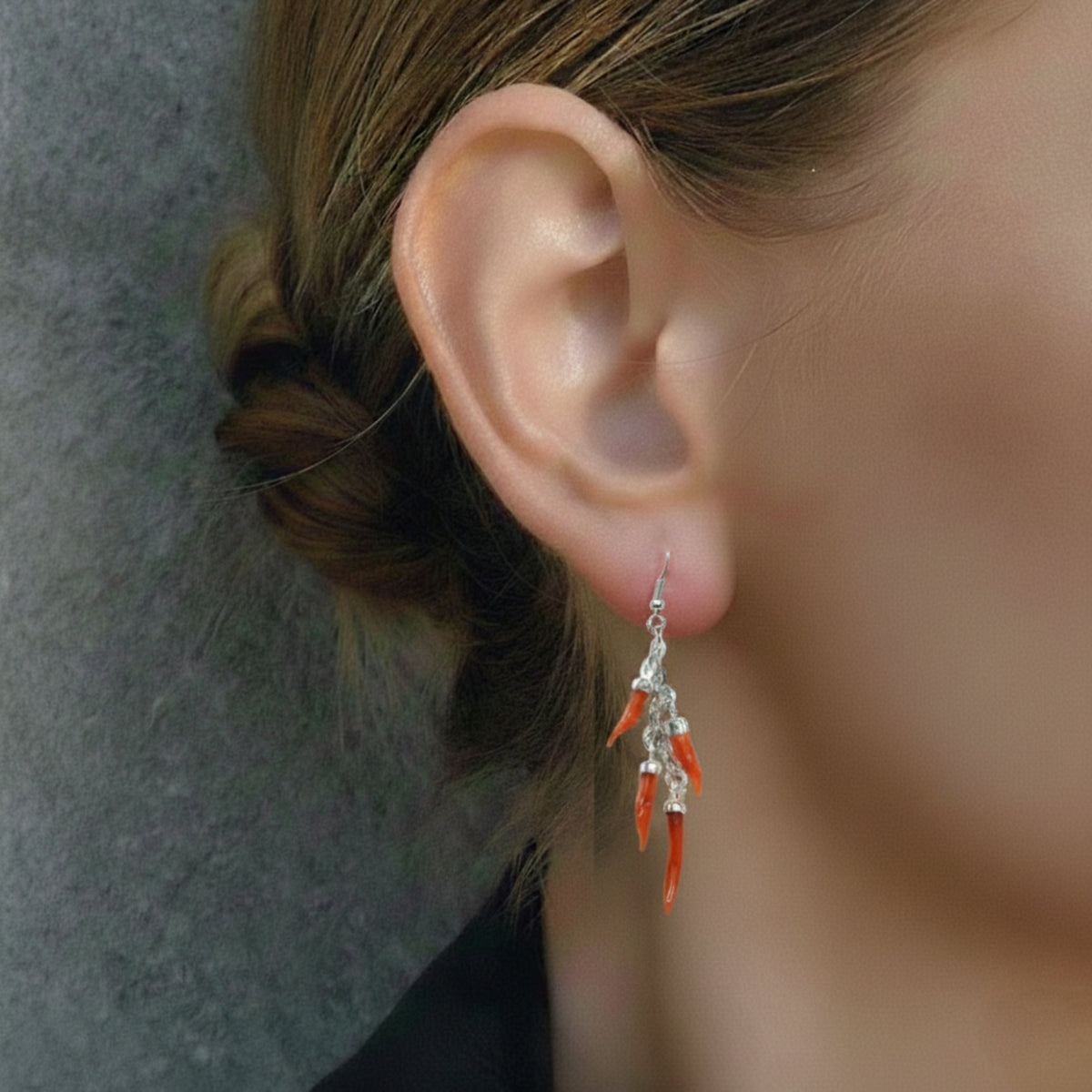 Orecchino pendente in argento con cornetti di corallo rosso, indossato in primo piano