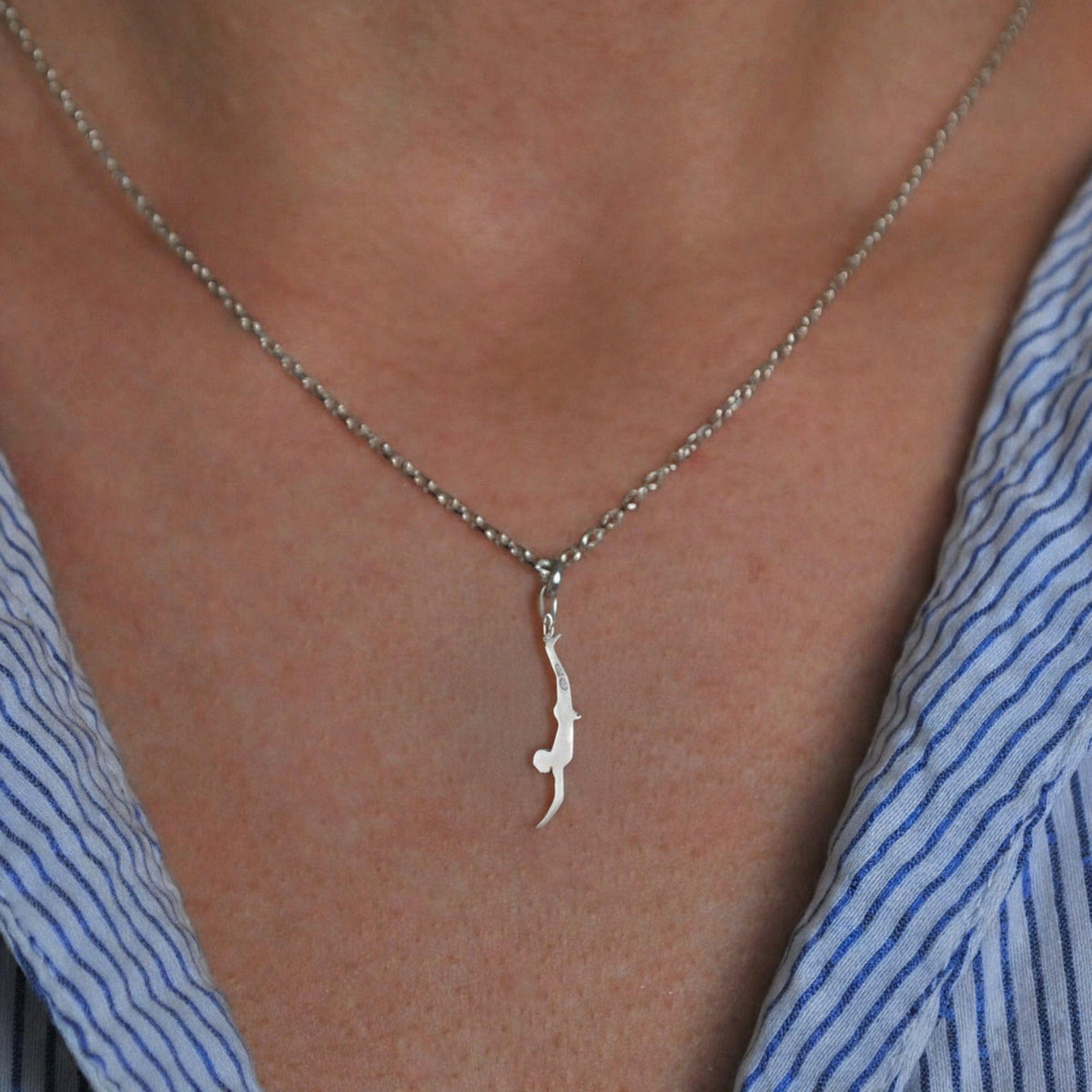 Pendente Tuffatore di Paestum piccolo in argento, indossato con una camicia a righe blu