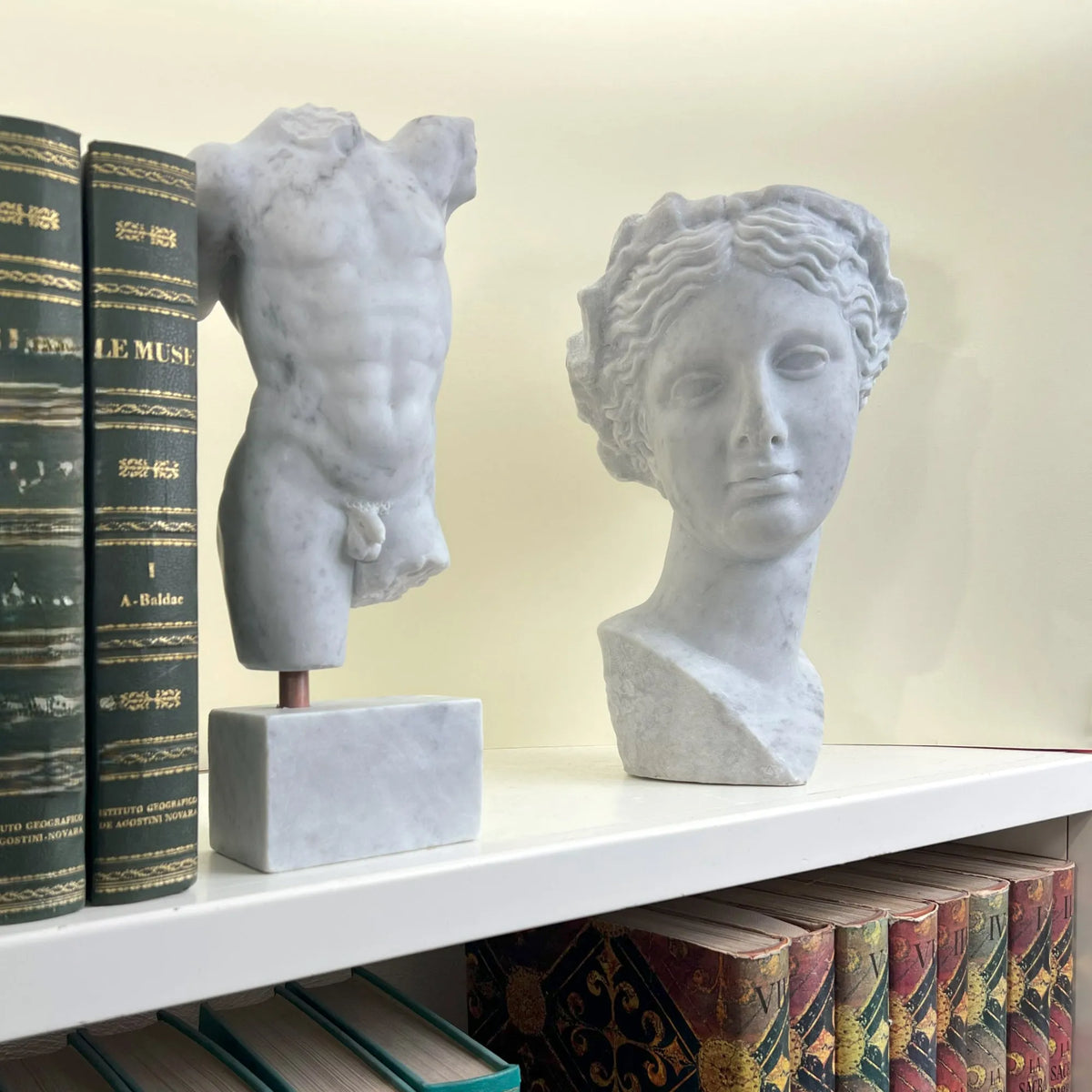 Riproduzione della scultura del torso di Perseo in marmo di Carrara, vista a tre quarti in una libreria. Affiancato dalla testa di Thalia Musa della Commedia.