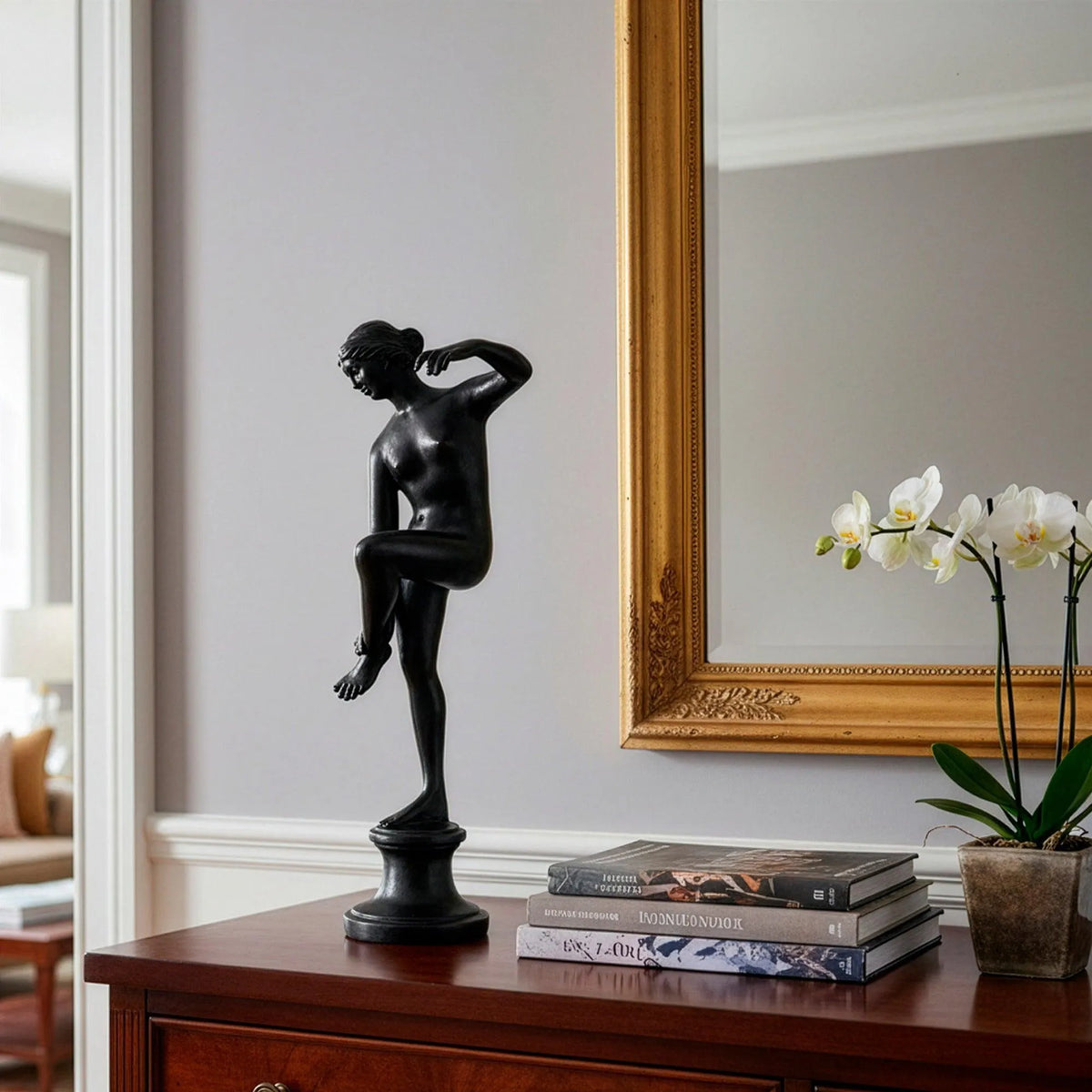 Venere al bagno in bronzo, statua decorativa con finitura scura lucida, figura femminile in posa elegante su base rotonda, ambientata in un interno raffinato.