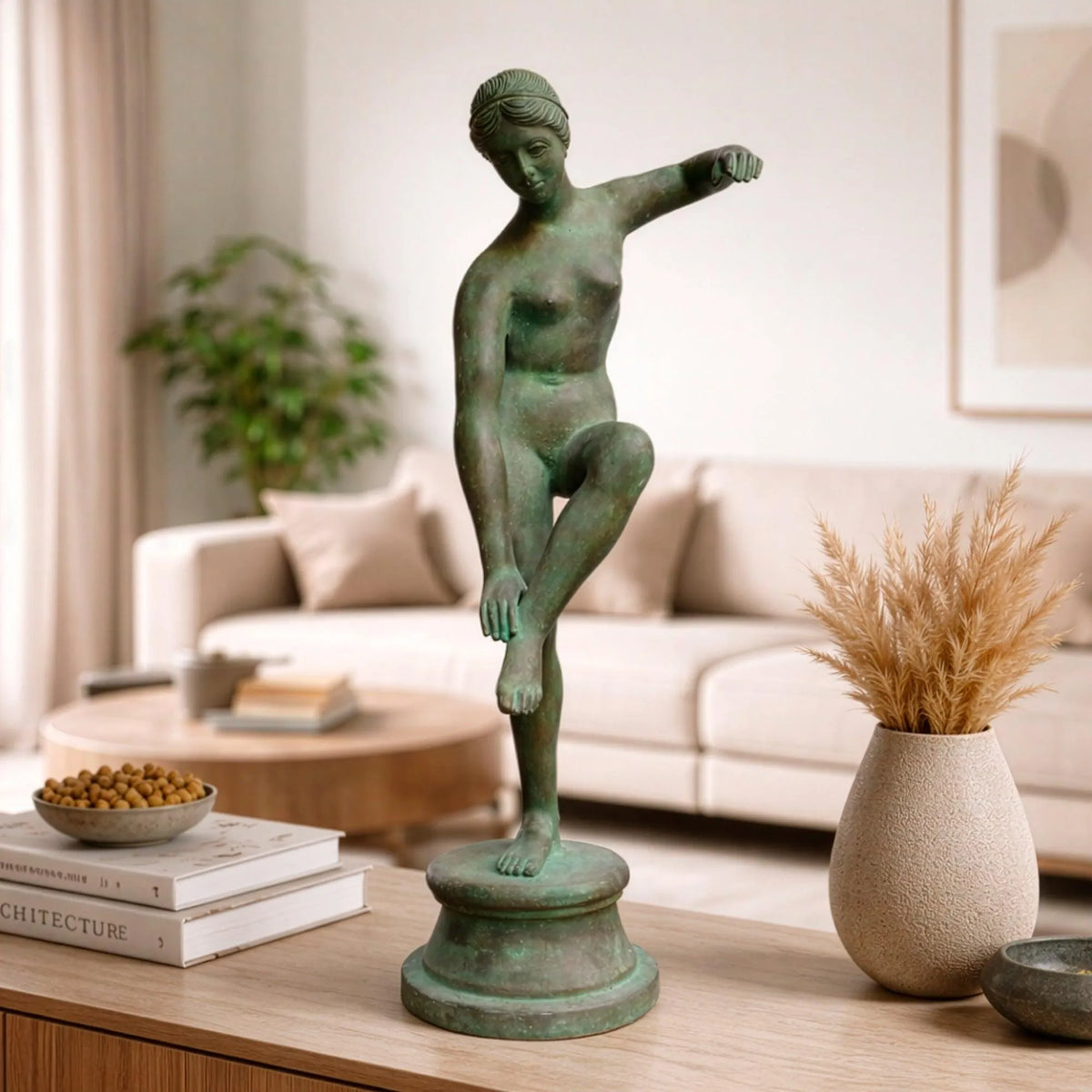 Venere al bagno in bronzo con patina verde, su un mobile in legno davanti a un divano chiaro.