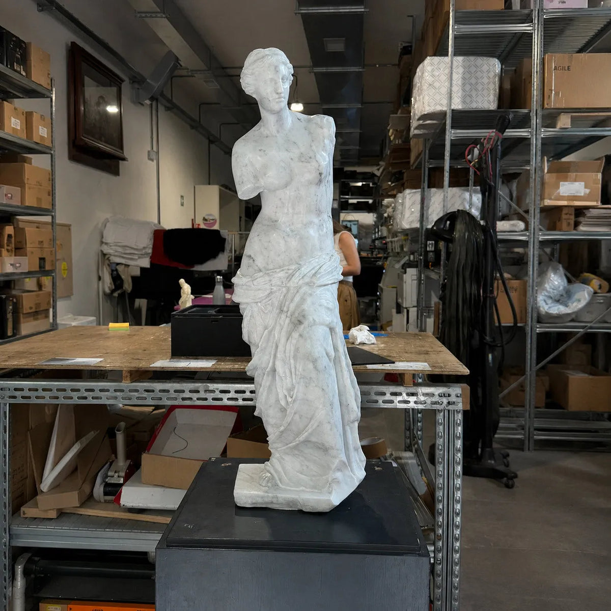 Venere di Milo in marmo di Carrara, vista frontale su piedistallo nero in laboratorio.