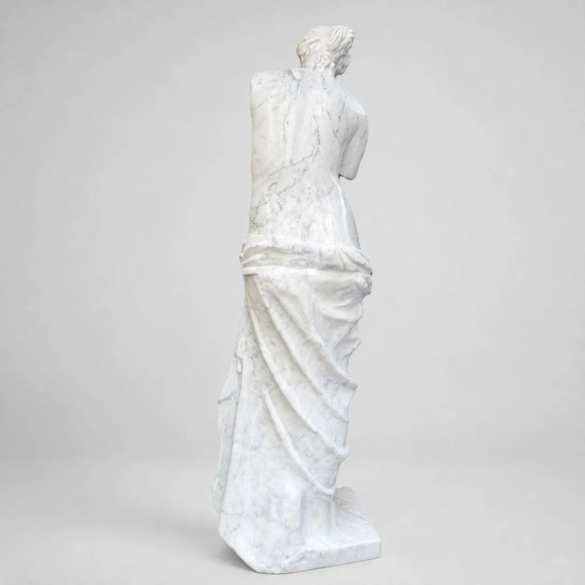 Venere di Milo in marmo di Carrara, vista posteriore su fondo grigio chiaro.