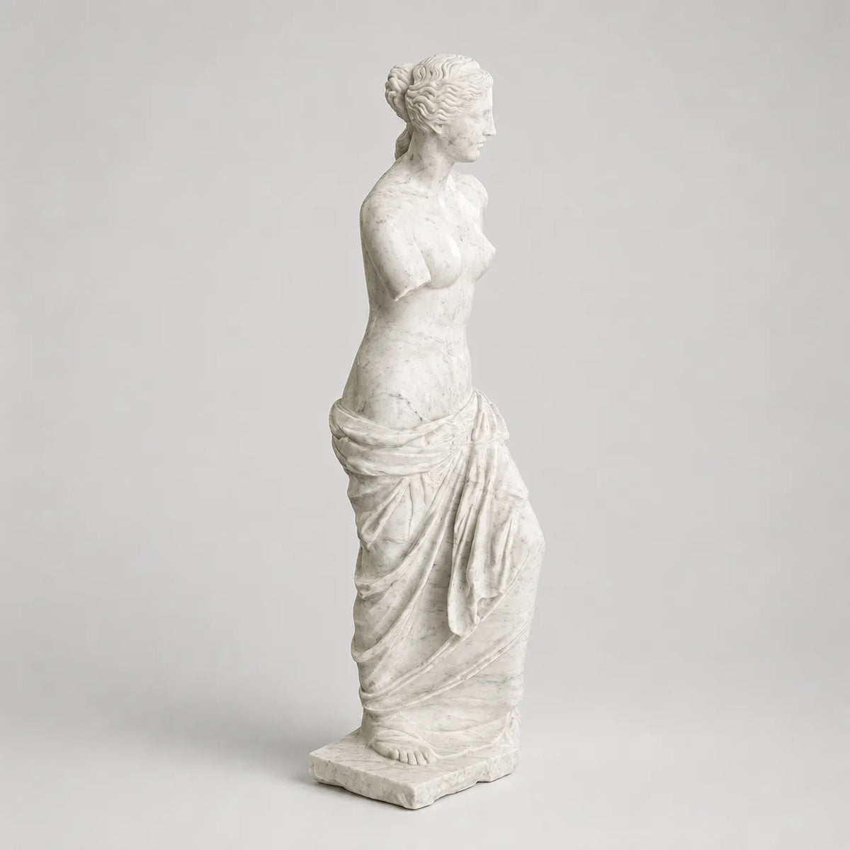 Venere di Milo in marmo di Carrara, vista di profilo su fondo grigio chiaro.