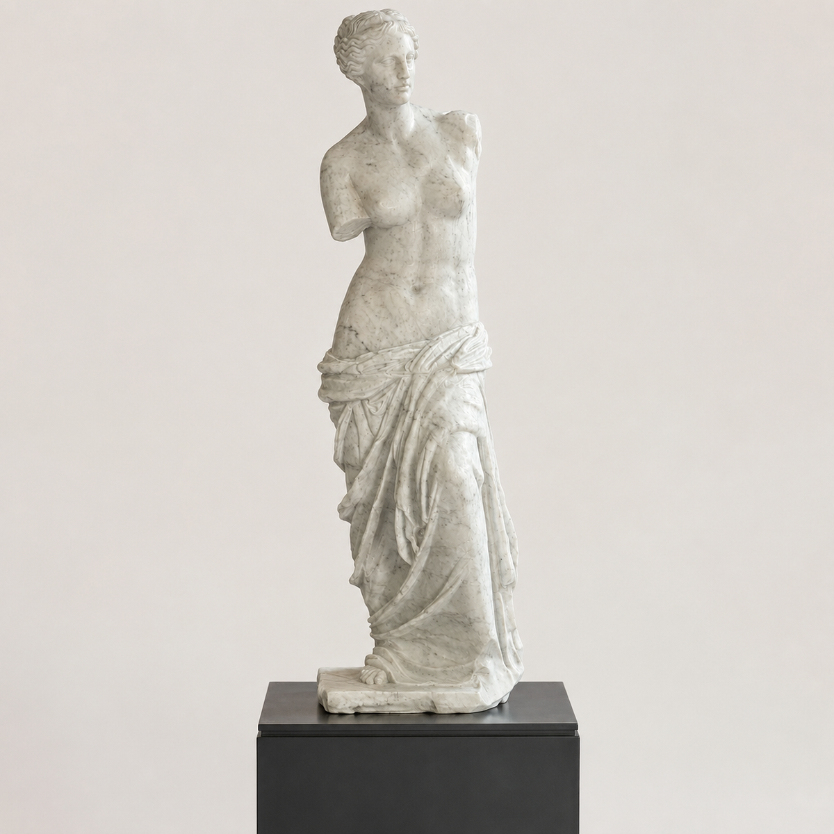Venere di Milo in marmo di Carrara, su piedistallo nero, vista frontale su fondo chiaro.