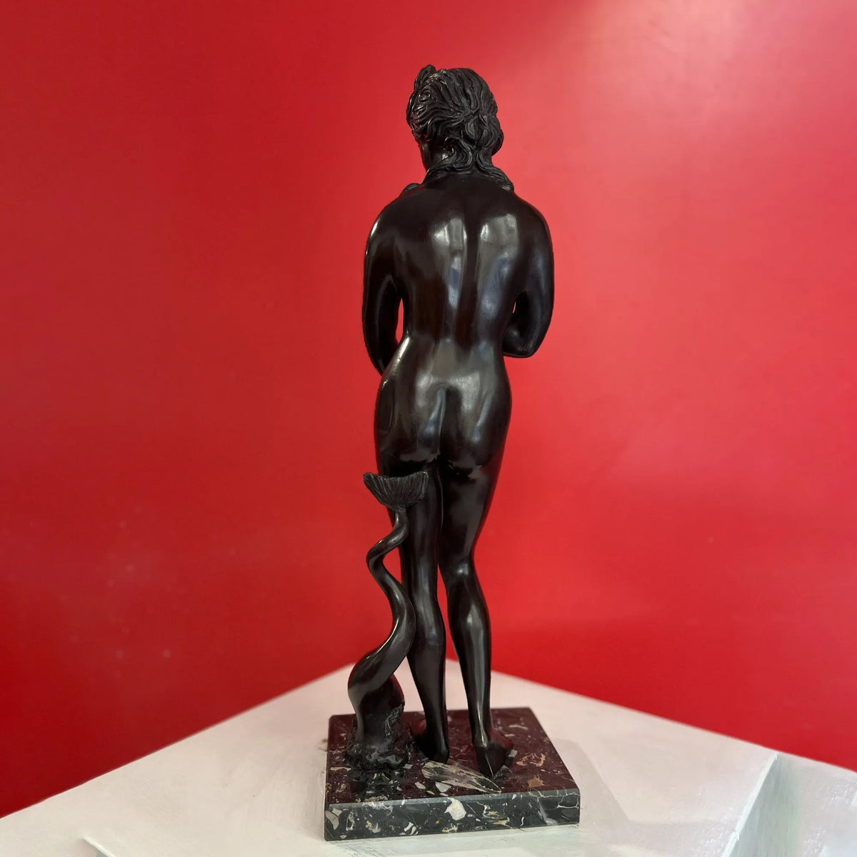 Venere dei Medici in bronzo scuro su base quadrata, vista posteriore davanti a una parete rossa.