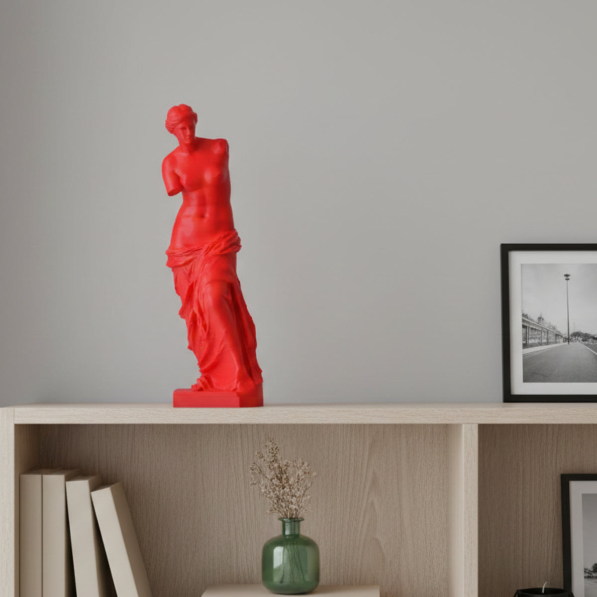 Venere di Milo rossa su un mobile in legno chiaro, accanto a una fotografia incorniciata.