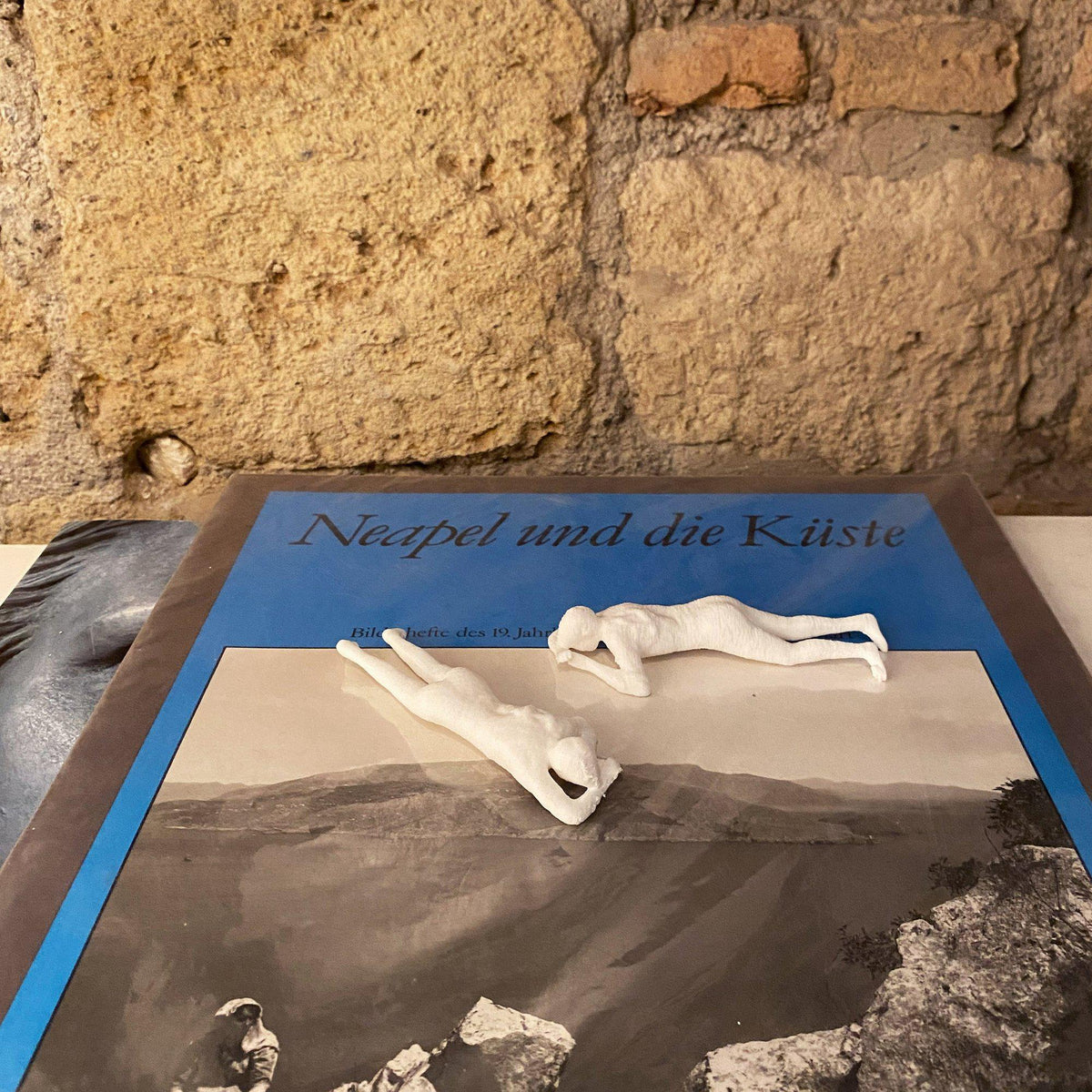 Due riproduzioni bianche del calco di donna stesa in PLA appoggiate su un libro illustrato.