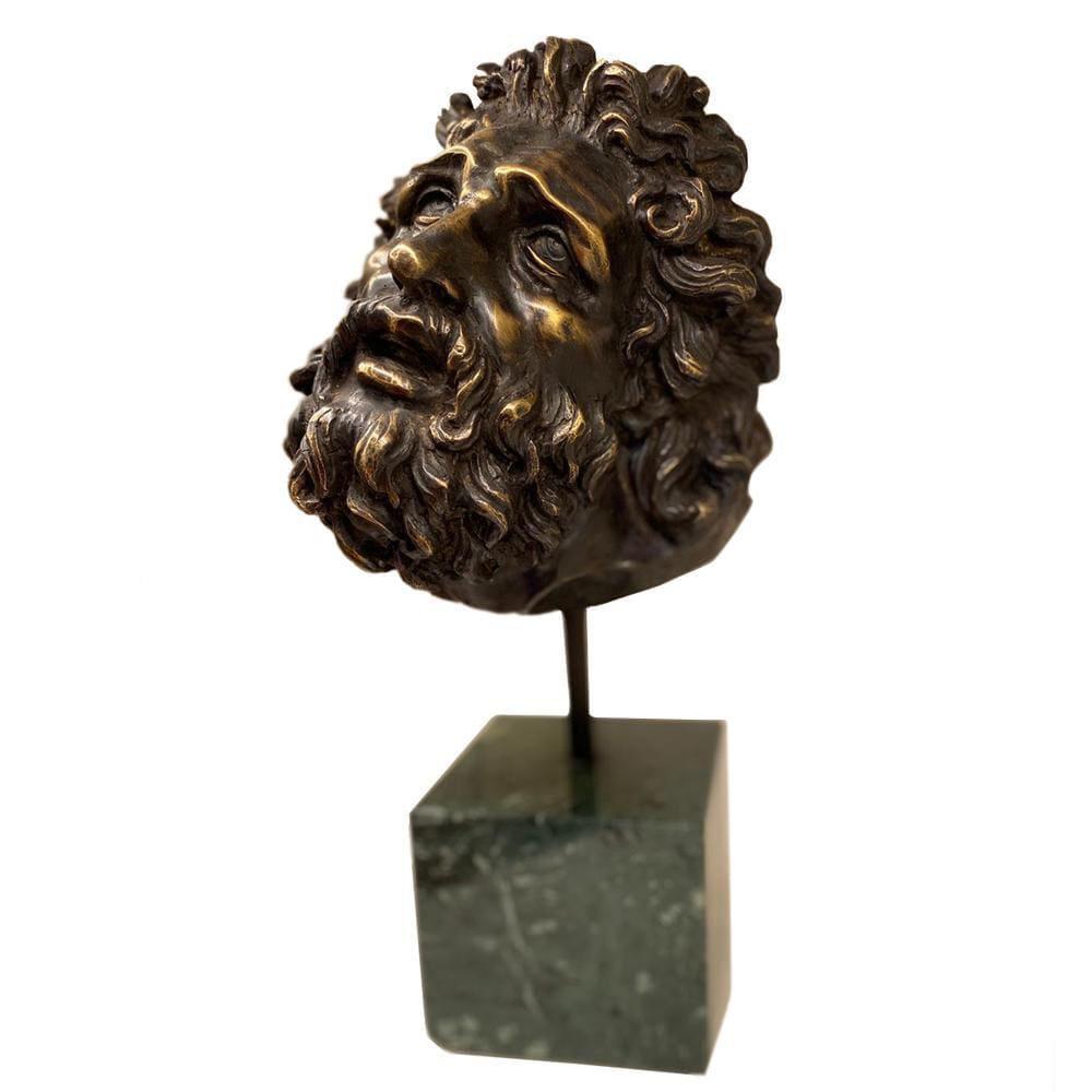 Cabeza del Laocoonte en bronce sobre base de mármol verde, fotografiada de perfil con detalles de la barba, del cabello rizado y del rostro expresivo.