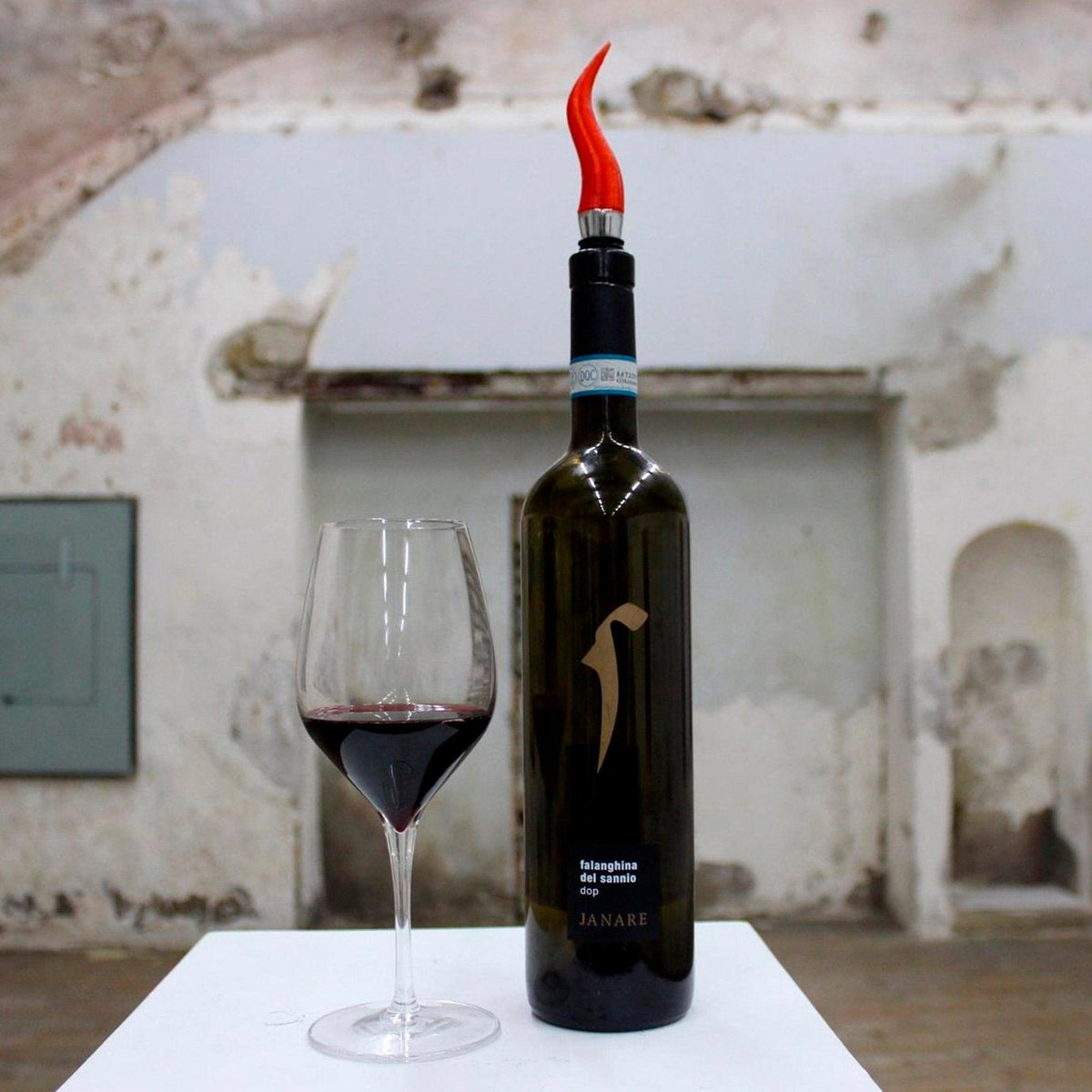 Tappo a corno napoletano rosso su una bottiglia accanto a un calice di vino rosso.