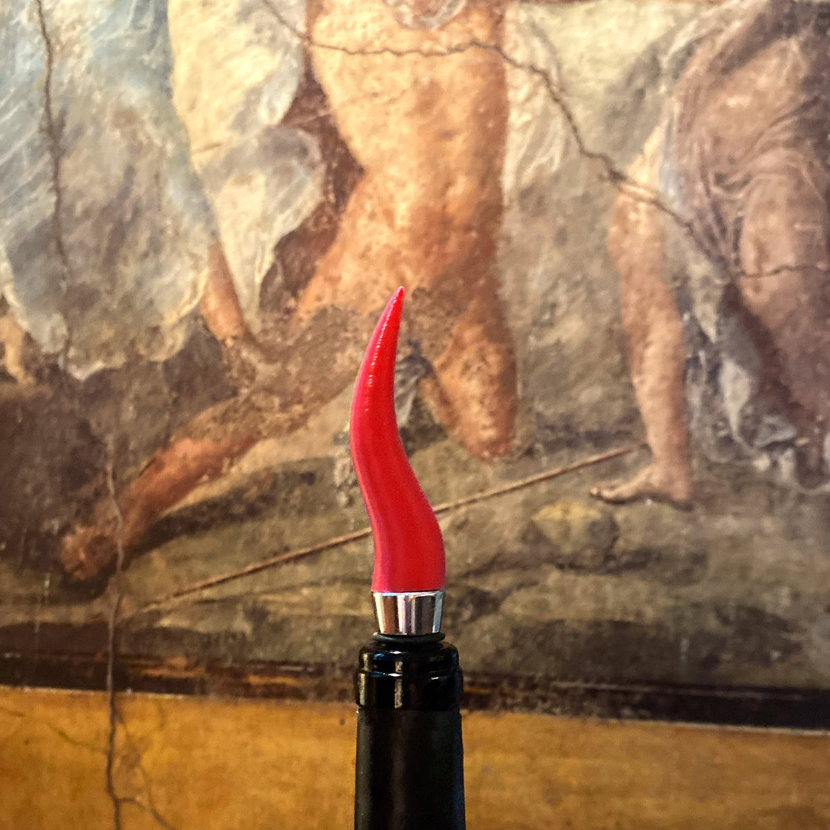 Dettaglio del tappo a corno napoletano rosso su una bottiglia, davanti a una parete dipinta.